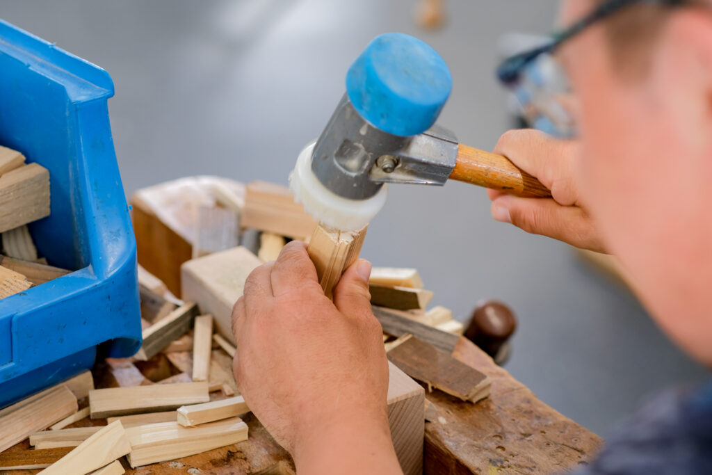 Nahaufnahme einer handwerklichen Arbeit in der Werkstatt des Lebensbaum in Osterode mit einem Hammer und Holzstücken